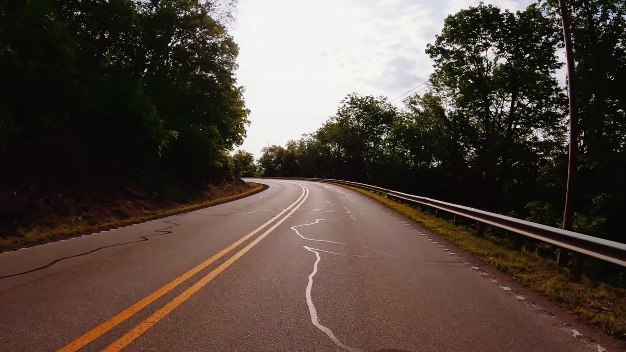 A black Mazda MX-5 roadster, roof down, on a tree-lined road